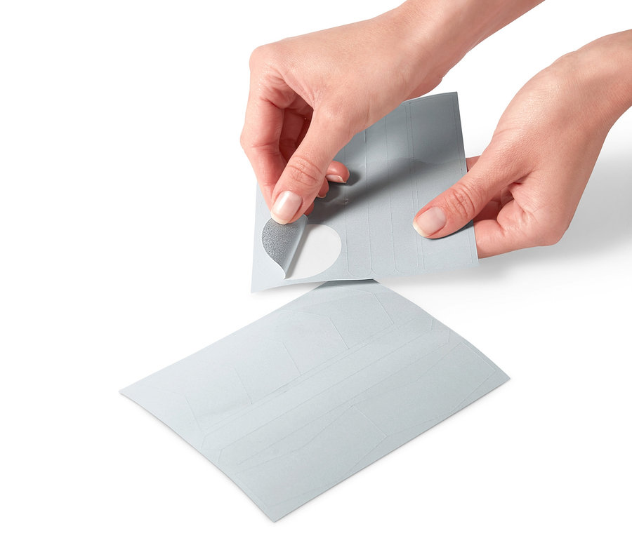 Des mains décollent un autocollant réfléchissant d'une planche de 16 autocollants réfléchissants.