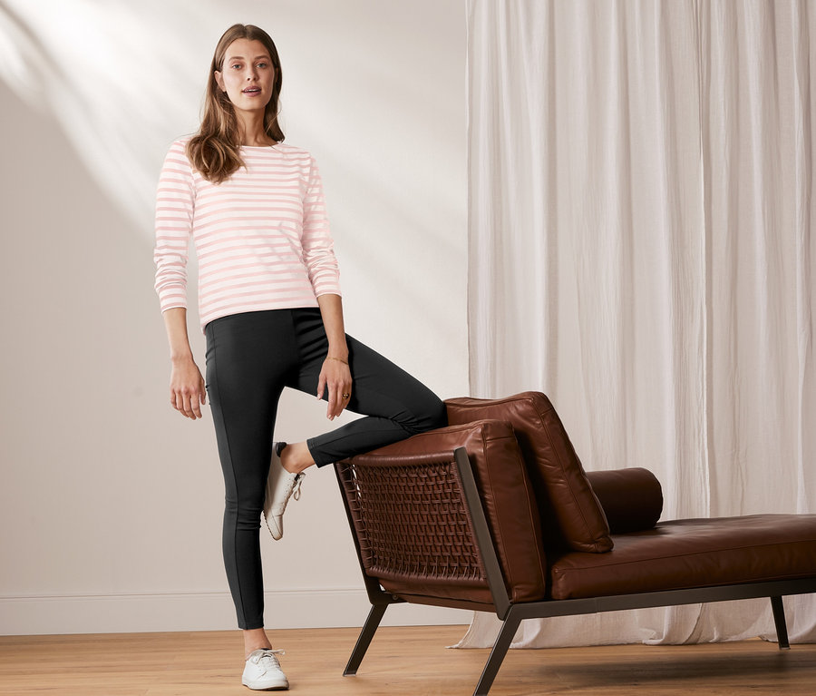 Une femme pose une jambe sur une méridienne en cuir. Elle porte un t-shirt manches longues à rayures rose et blanc et un legging épais.