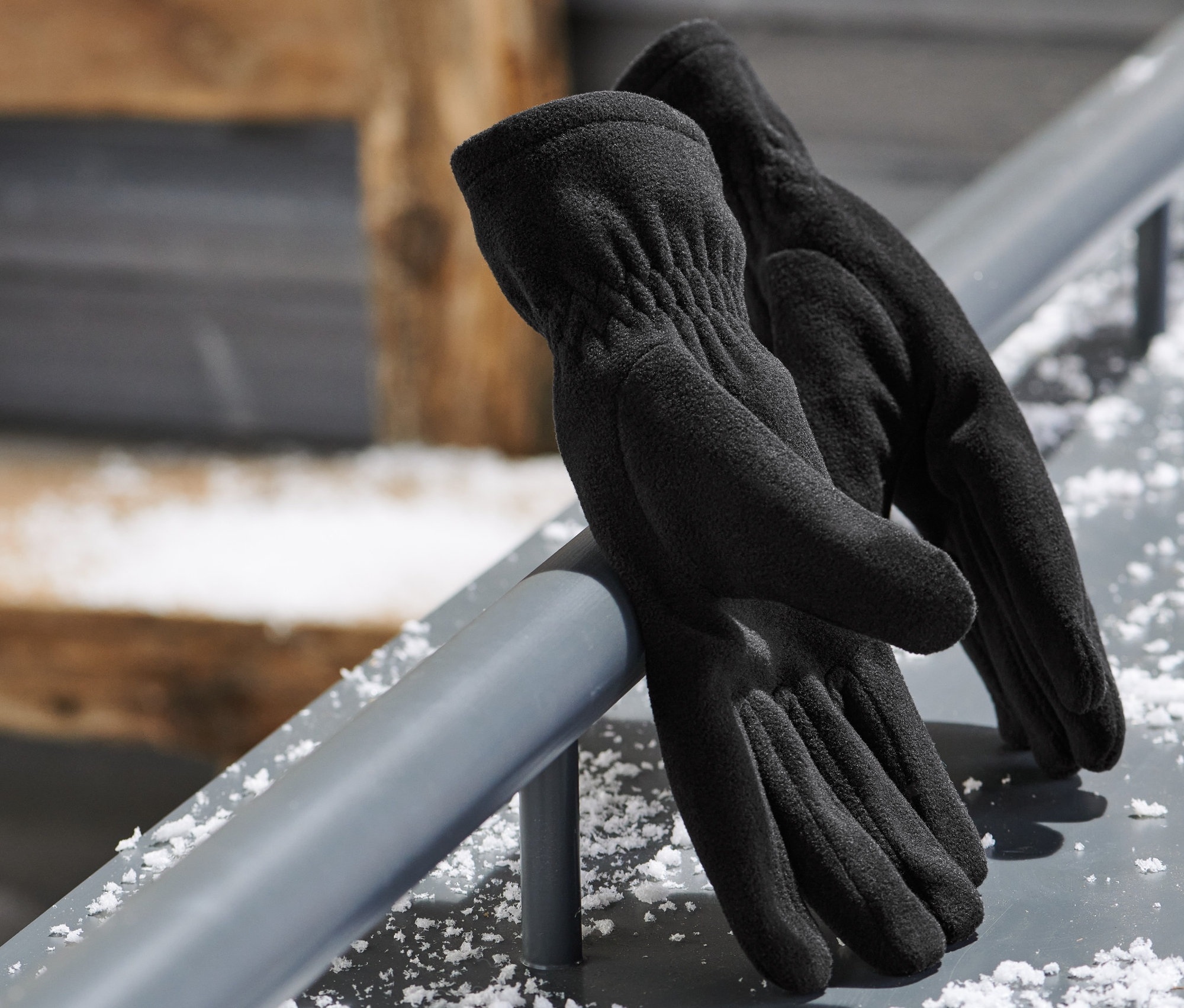 Des gants noirs en micropolaire sont posés sur une barre métallique. À l'arrière-plan, on aperçoit des lunettes de ski.