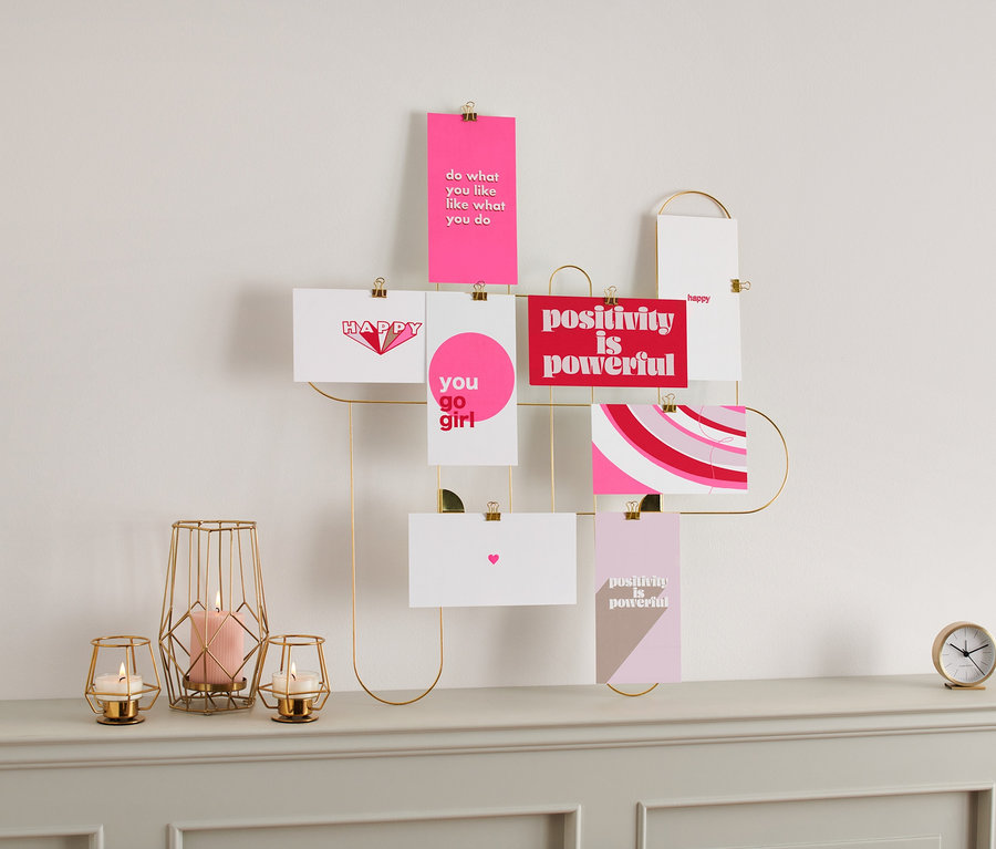 Un lot de cartes postales / mini cartes illustrées est accroché au mur sur un cadre doré. Des bougies et une horloge sont posées sur une commode.