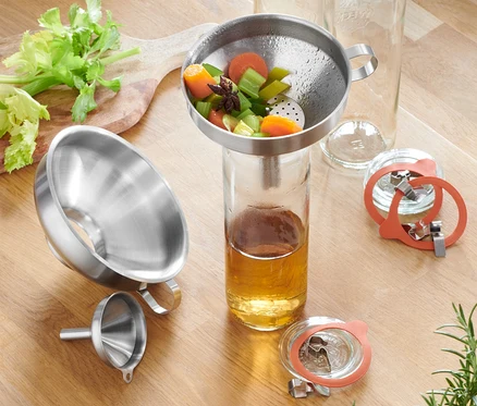 Ensemble d'entonnoirs en acier inoxydable sur une table en bois avec du céleri, des carottes, des verres et des épices.