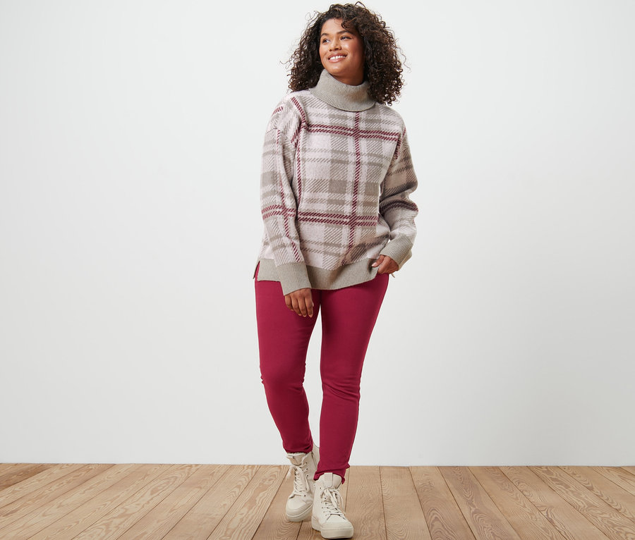 Une femme debout portant un pull en maille à col roulé et un jegging.