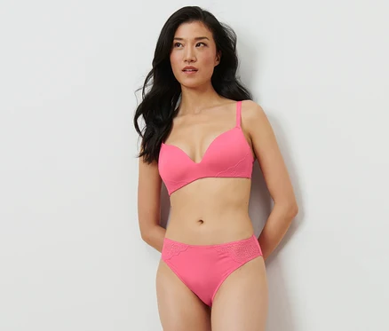 Une femme pose en portant un soutien-gorge rose et 2 slips, rose vif.