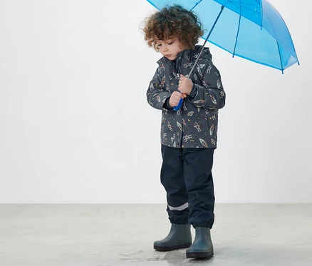 Garçon tenant un parapluie bleu et portant une veste de pluie thermique pour enfant bleu foncé.