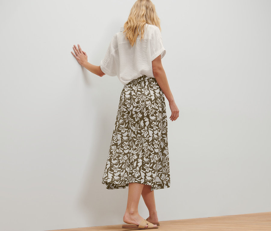 Femme posant en jupe midi imprimée et chemise blanche.