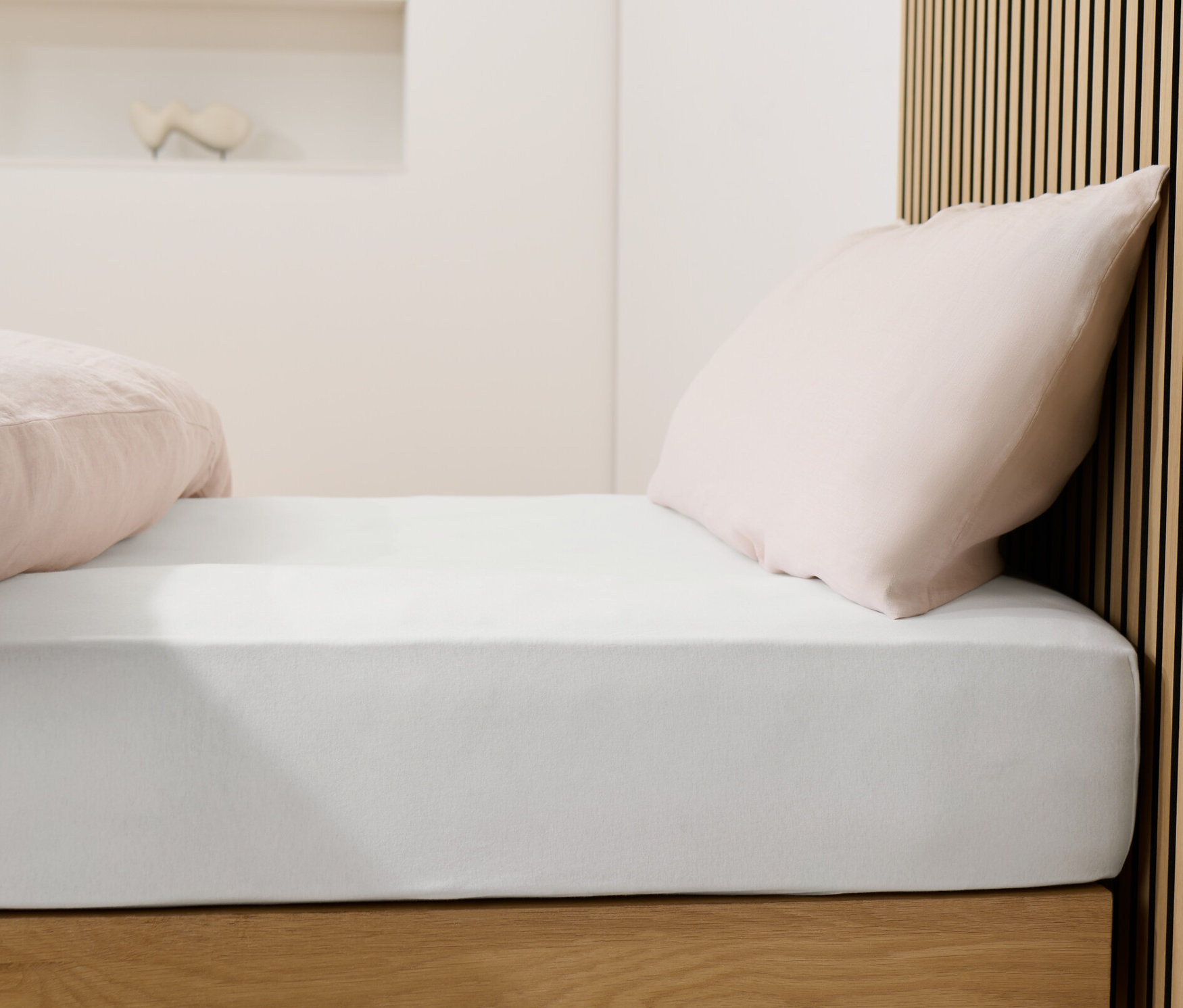 Lit avec drap-housse en jersey blanc et oreillers roses.