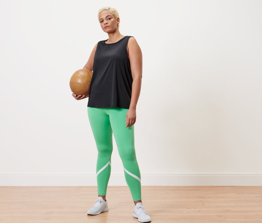 Femme tenant un ballon de volley-ball, portant un legging de sport vert et un débardeur de sport anthracite.