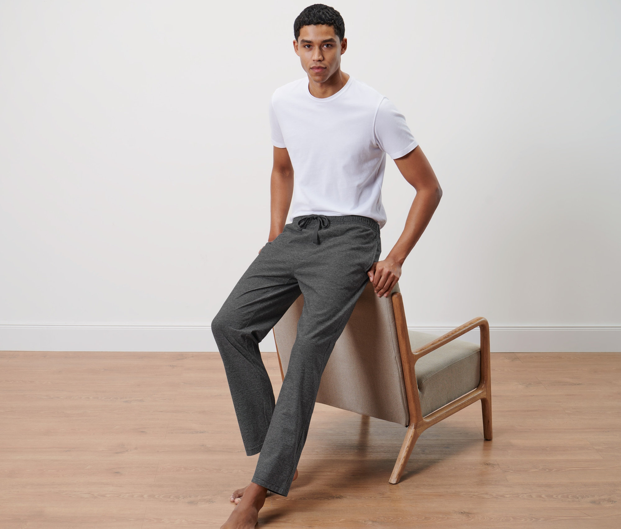 Un homme appuyé sur une chaise porte un t-shirt blanc et un pantalon de détente.