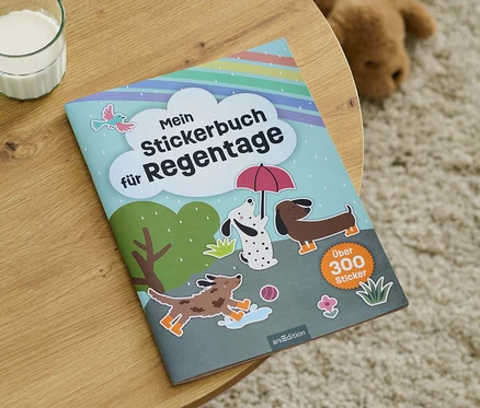 Sur une table en bois se trouve un « Mein Stickerbuch für Regentage » à côté d'un verre de lait.