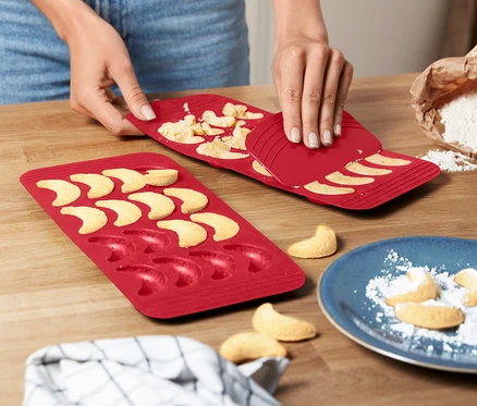 Une femme démoule des croissants à la vanille d'un 2	apis de cuisson rouge pour croissants vanillés.