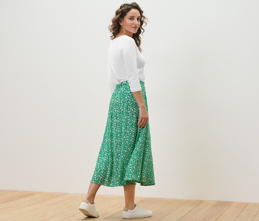 Femme posant dans une jupe midi imprimée verte et un haut blanc.