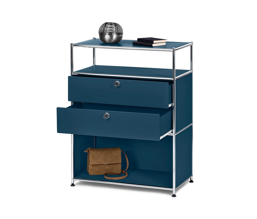 Une commode bleue « CN3 » avec 2 tiroirs dont un ouvert. Sur l'étagère supérieure se trouvent des décorations et des livres et sur l'étagère inférieure un sac à main marron.