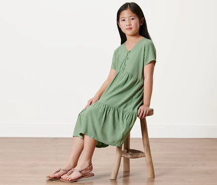 Une fille est assise sur un tabouret et porte une robe étagée pour enfant.