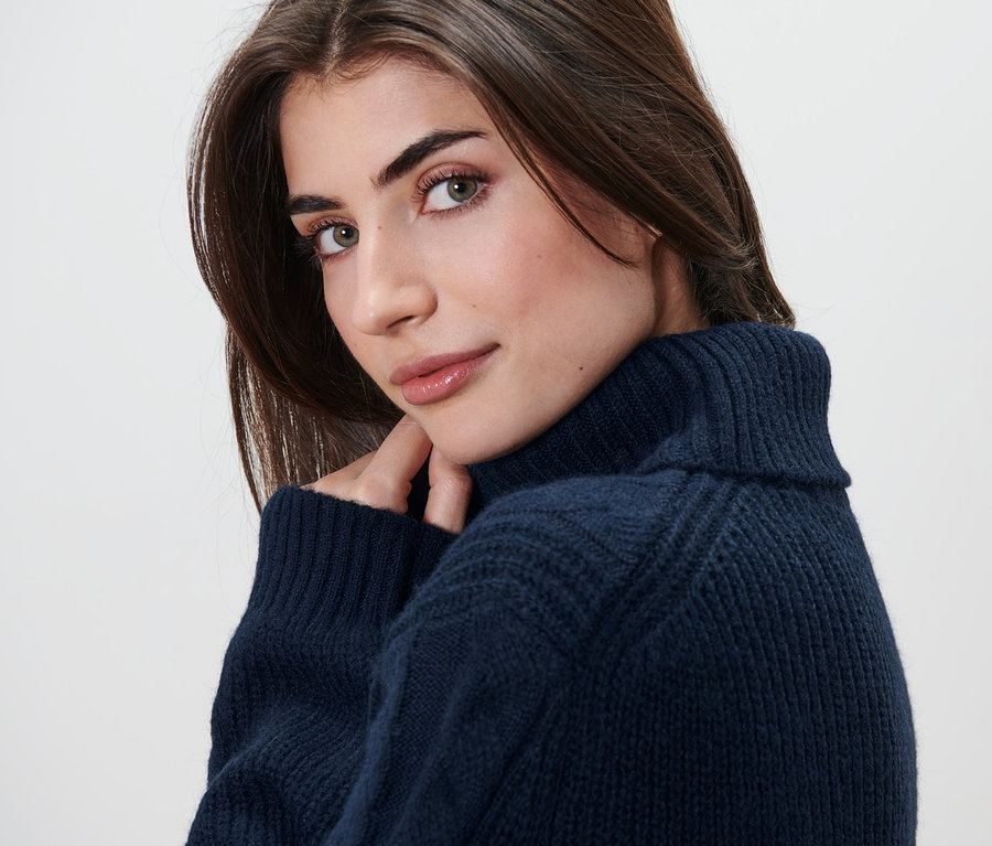 Une femme regardant par-dessus son épaule portant un long pull en maille avec torsades.