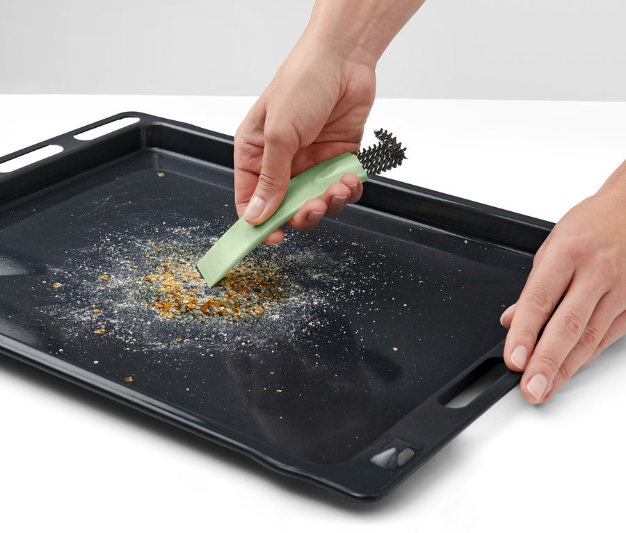 Des mains nettoient une plaque de cuisson noire avec une brosse à four avec racloir.