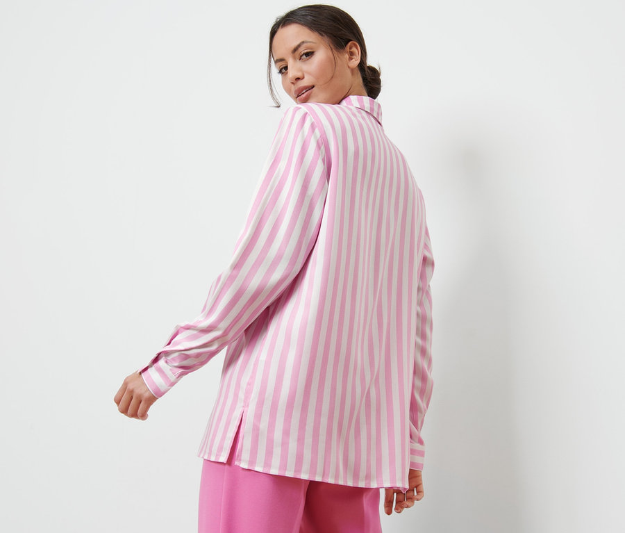 Femme regardant par-dessus son épaule portant une blouse rayée rose.