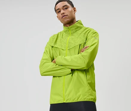 Un homme, les bras croisés, porte une veste de course coupe-vent vert fluo.