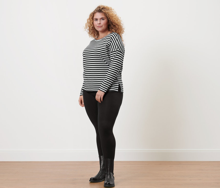 Femme portant un t-shirt à manches longues rayé, un legging noir et des bottes noires.