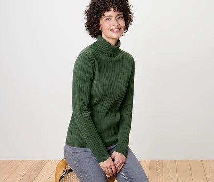 Une femme est assise sur une chaise et porte un pull à col roulé côtelé vert.