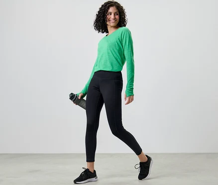 Femme portant un legging thermique et un t-shirt vert tenant une bouteille d'eau.