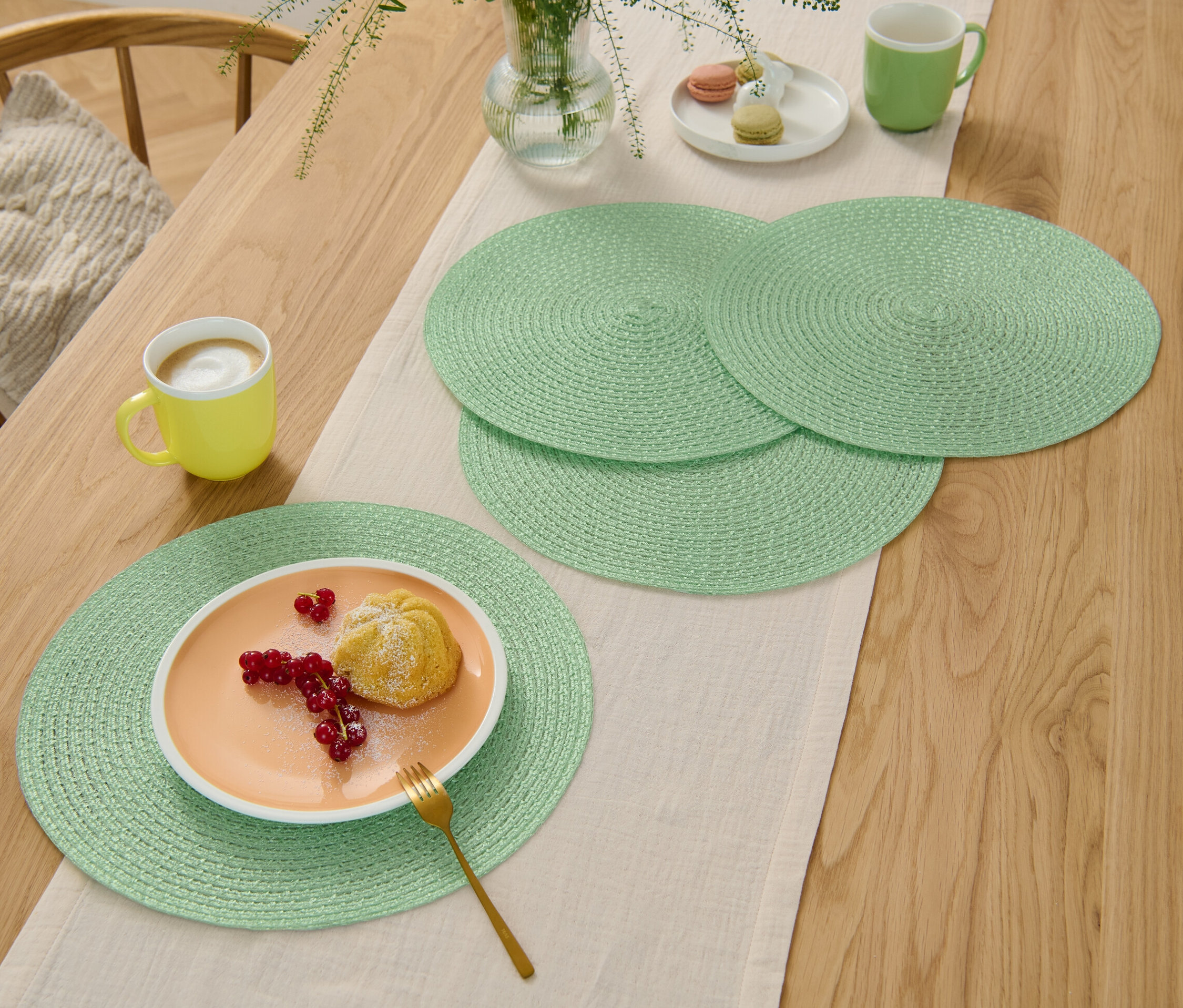 Quatre sets de table verts sur une table en bois avec un chemin de table, une assiette avec un dessert.