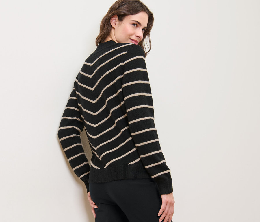 Une femme regarde par-dessus son épaule et porte un pull rayé en maille à col montant, noir.