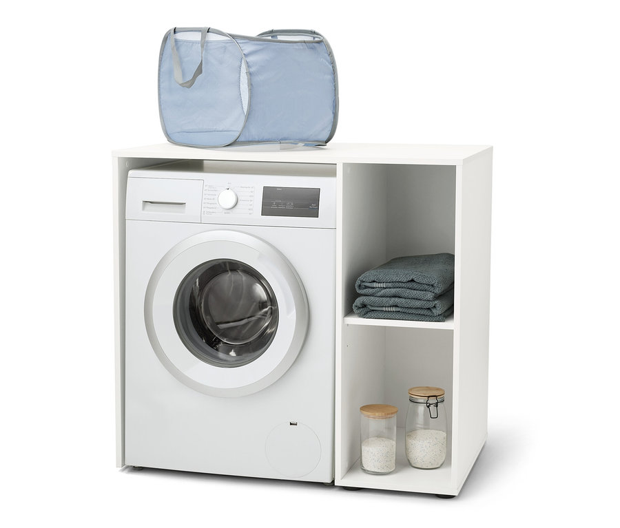 Une machine à laver est placée dans une étagère pour machine à laver blanche avec espace de rangement latéral. Un panier à linge bleu est posé sur la machine à laver.