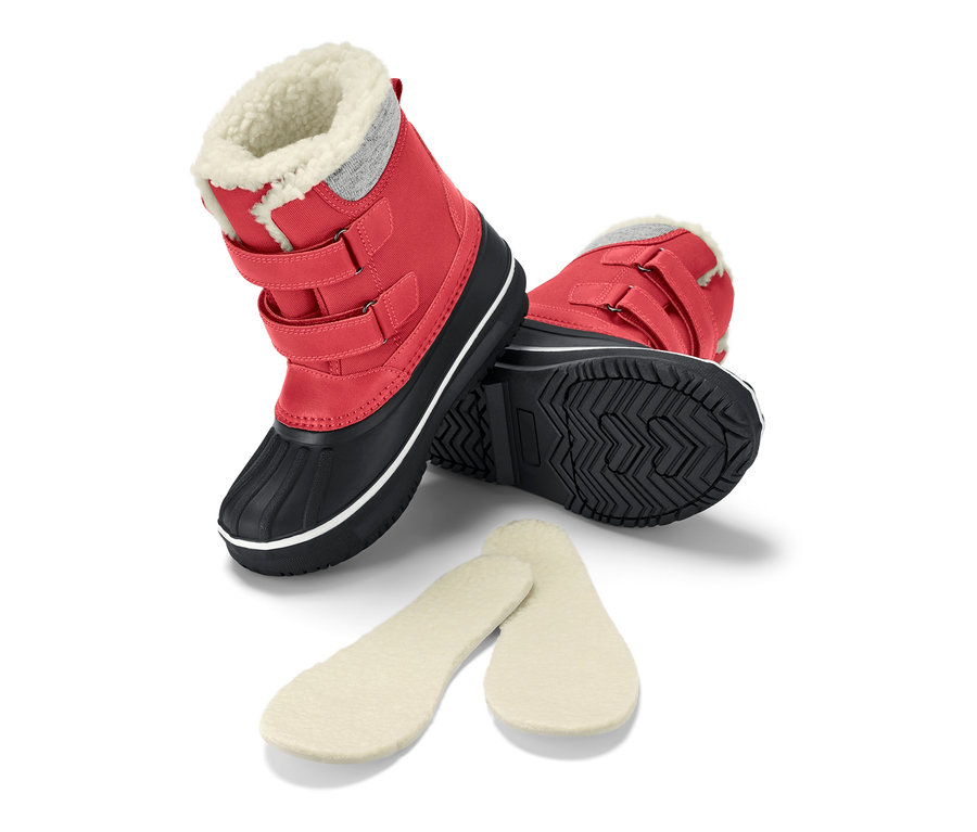 Une botte rouge pour enfant est posée sur le côté, avec des semelles à côté.