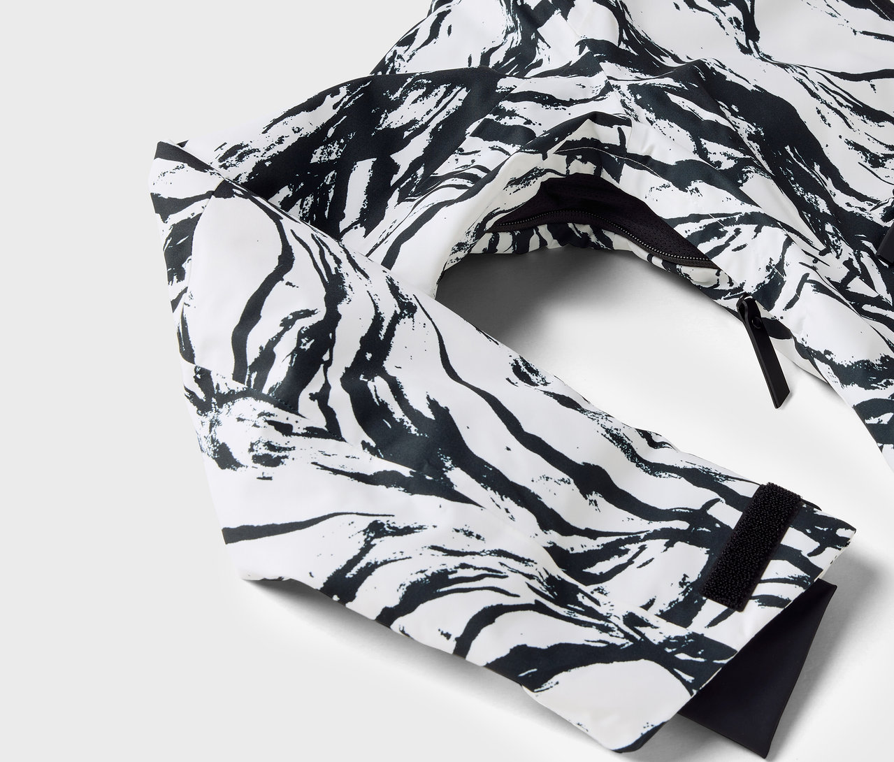 Gros plan sur une veste blanche à motif noir, avec la manche et la fermeture éclair visibles.