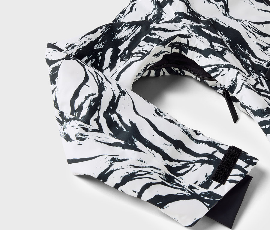 Gros plan sur une veste blanche à motif noir, avec la manche et la fermeture éclair visibles.