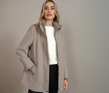 Femme portant un manteau court Street One beige, combiné avec un haut blanc et un pantalon noir.