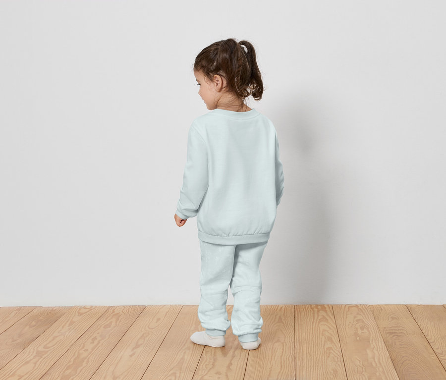 Une petite fille se tient dos à la caméra et porte un survêtement bleu clair.