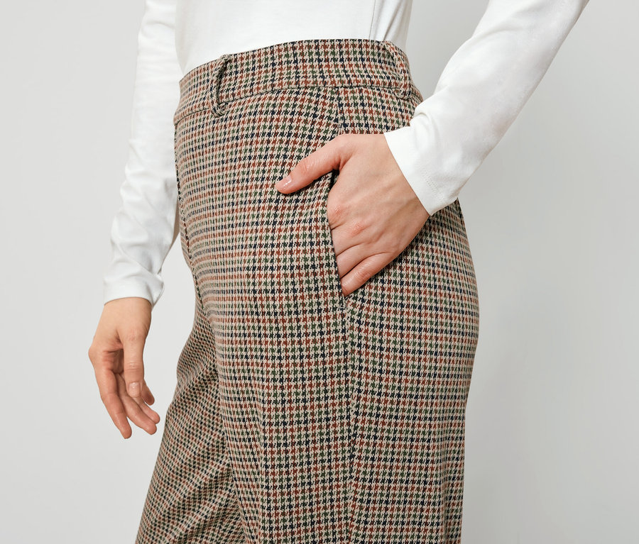 Une femme a sa main dans la poche d'un pantalon à carreaux marron.