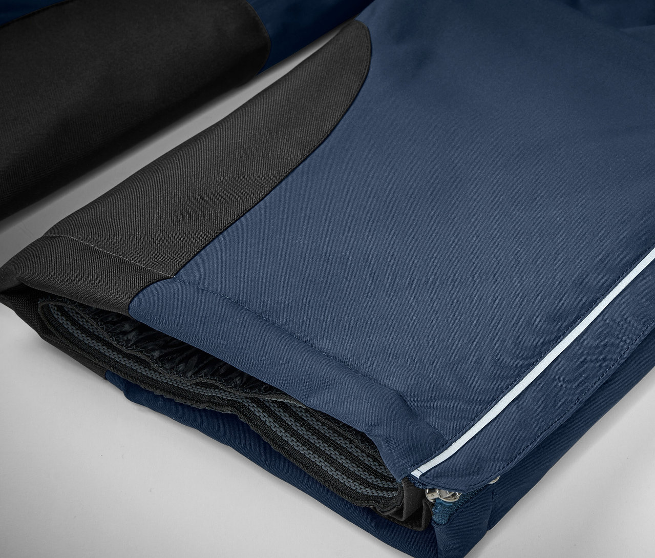 Détail d'un pantalon bleu avec des détails noirs et une bande blanche.