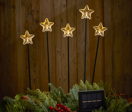Cinq étoiles lumineuses sur des bâtons dans une couronne verte avec des pommes de pin et des baies rouges devant un fond en bois.