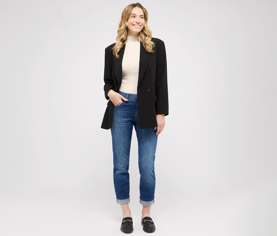 Une femme porte un jean Angels « Darleen TU », coupe croisée 7/8, un haut et un blazer, et se tient debout.