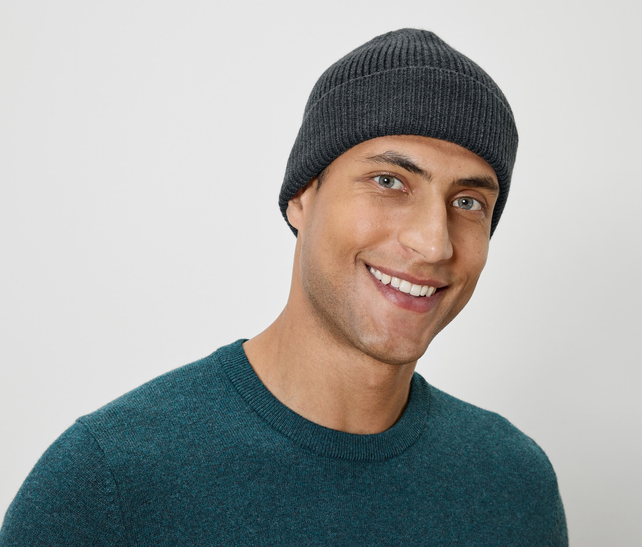 Portrait d'un homme souriant portant un bonnet en tricot gris et un pull vert.