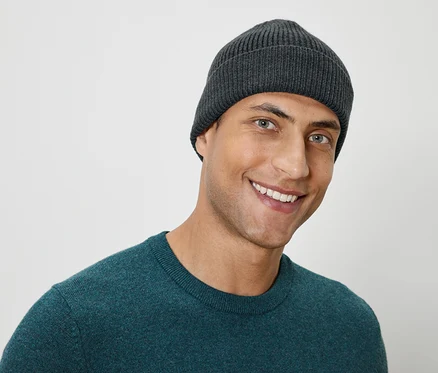 Portrait d'un homme souriant portant un bonnet en tricot gris et un pull vert.