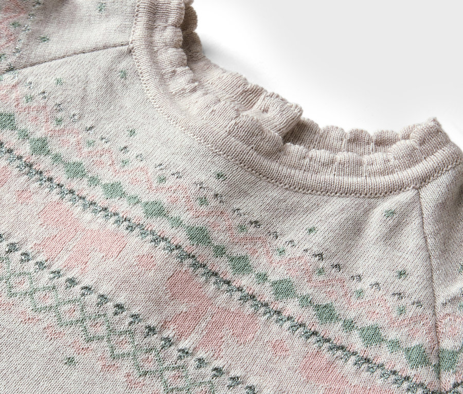 Détail d'un pull avec motif rose et vert et encolure à volants.