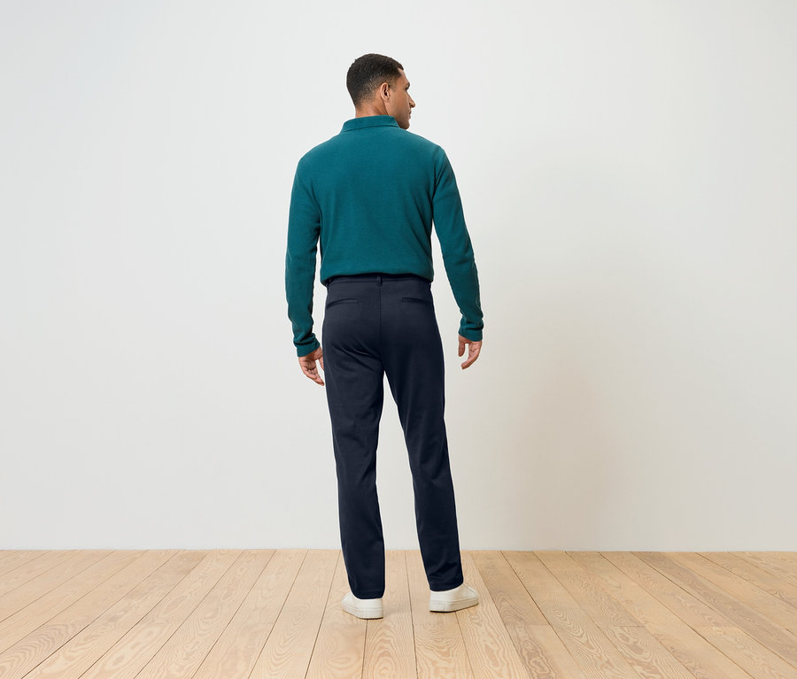 Un homme, vu de dos, porte un pantalon bleu et un haut vert à manches longues.