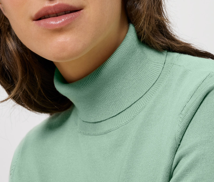 Gros plan d'une femme aux cheveux bruns portant un pull à col roulé vert menthe.