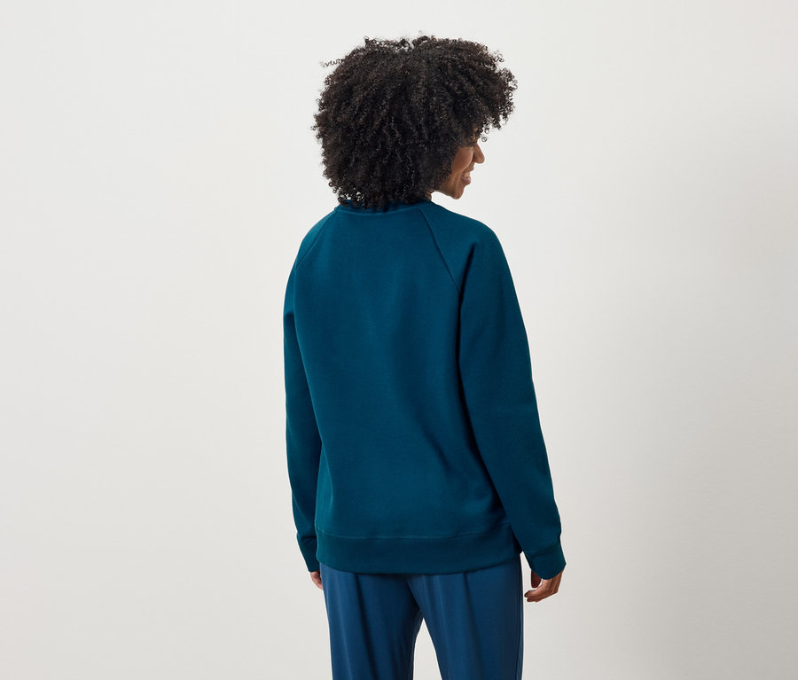 Vue arrière d'une femme aux cheveux bouclés portant un pull et un pantalon bleus.