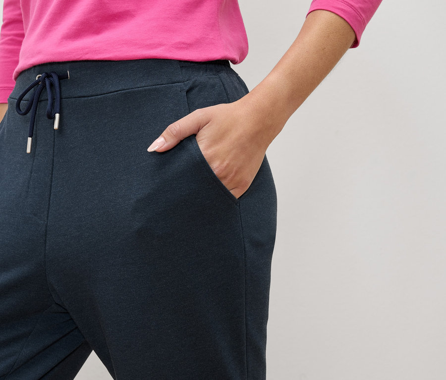 Gros plan d'une personne portant un pantalon de jogging bleu marine avec cordon de serrage et poches, une main dans la poche.