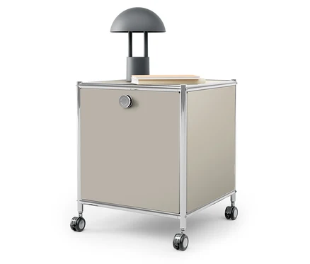 Sur le dessus d'un caisson beige à roulettes se trouvent une lampe grise et un livre.
