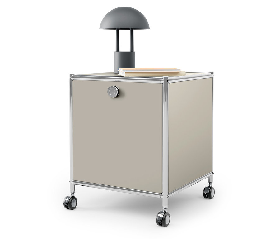 Sur le dessus d'un caisson beige à roulettes se trouvent une lampe grise et un livre.