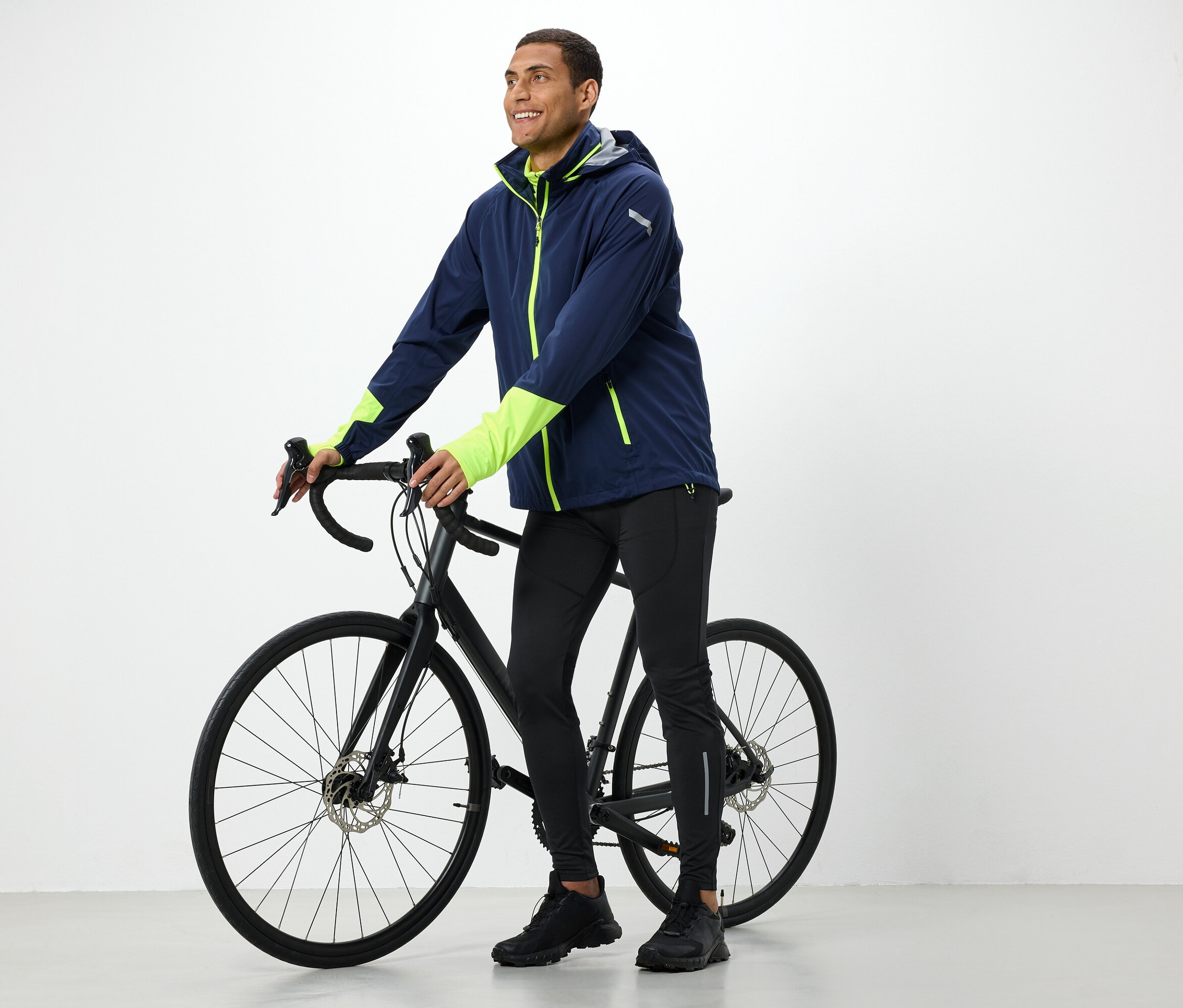 Un homme en veste tient un vélo noir.