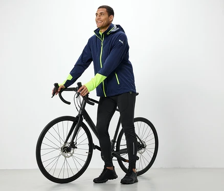 Un homme en veste tient un vélo noir.