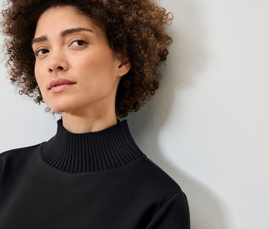 Portrait d'une femme aux cheveux bouclés portant un pull noir à col roulé.