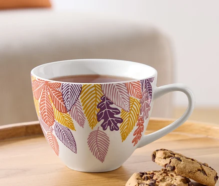 Une tasse de thé avec un motif de feuilles d'automne et deux biscuits au chocolat sur un plateau en bois.