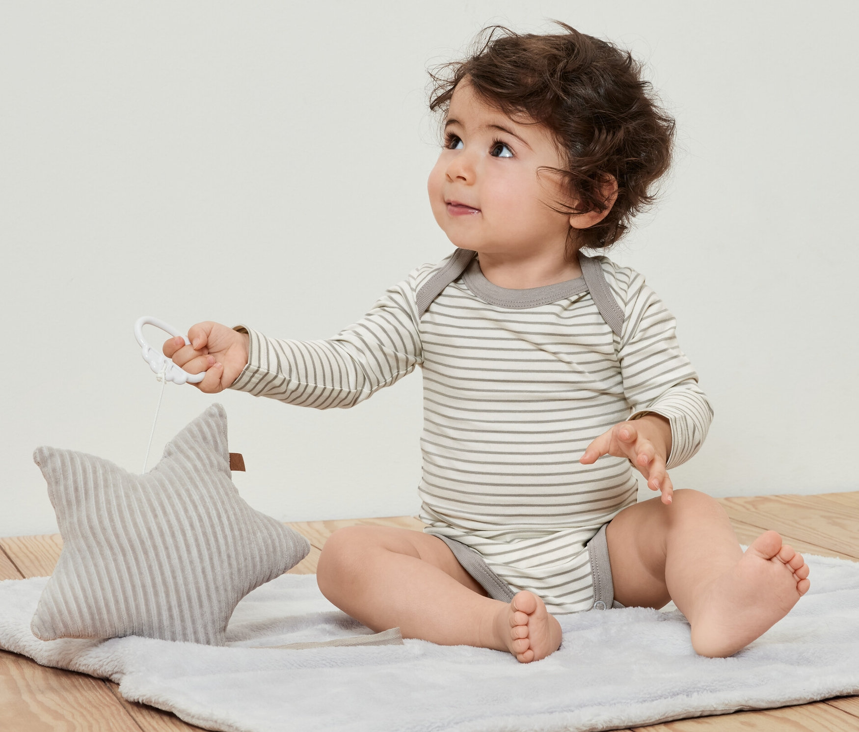 Un bébé bouclé est assis sur une couverture et joue avec une étoile. Il porte 5 bodys évolutifs pour bébé.